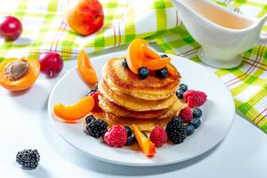 Stack of pancakes with fruit blueberries, raspberries, mulberry, apricot pieces and honey