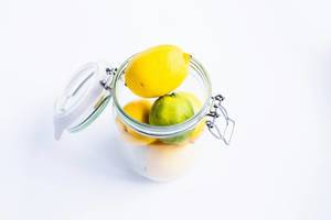 Stacked fresh lemons and lime in a metal jar on white background