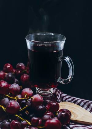 Steam above red grape tea in a glass, with ripe fruits