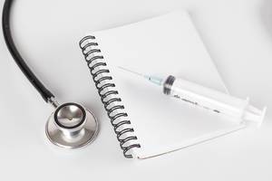 Stethoscope with notebook and syrige on white table