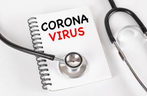 Stethoskop auf einem Notizbuch mit den Worten Corona Virus auf einem weißem Tisch