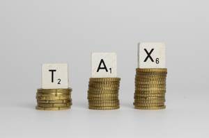 Steuern - Das Wort TAX geschrieben auf Holzblöcken auf Münzstapeln