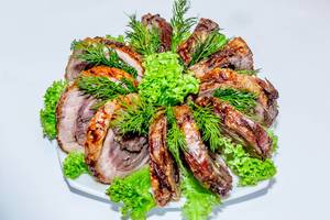 Stücke von Schweinefleisch-Roulade schön angerichtet mit Kräutern und Salaten vor weißem Hintergrund