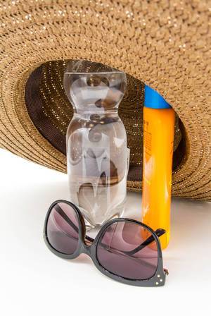 Sun glasses, bottle of water and sun cream under a strawhat