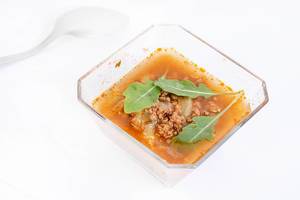 Suppe mit Hackfleisch und frischem Rucola in Glasschale vor weißem Hintergrund