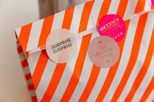 Surprise bag as a loving birthday gift in a white-orange striped paper bag with three round stickers