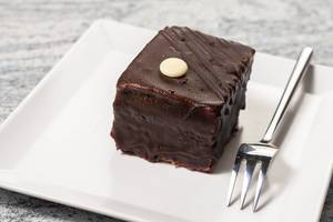 Süßes Schokoladentörtchen mit Glasur neben Kuchengabel auf Dessertteller