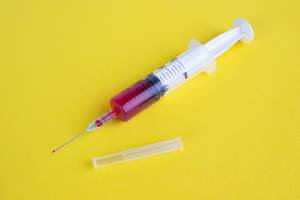 Syringe with blood on yellow background