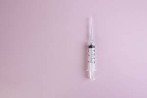Syringe with liquid on pink background