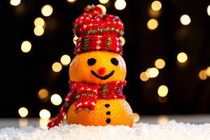 Tangerine snowman in the snow on a blurry background of luminous garlands