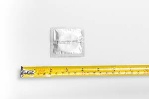 Tape measure and condom on a white background. Sizing concept
