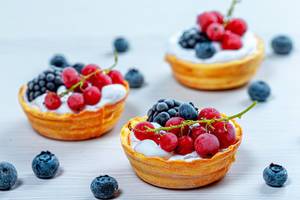 Tartlets with cream and fresh berries on a white wooden background (Flip 2019)
