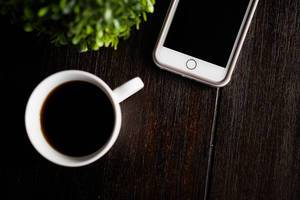 Tasse mit schwarzem Kaffee und IPhone auf einem rustikalen Holztisch