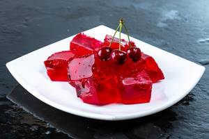 Tasty jelly cubes on white plate with cherry