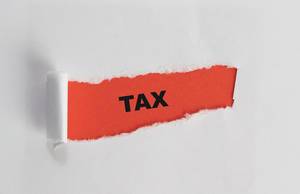 Tax: Englischer Begriff für Steuer auf rotem Untergrund unterhalb aufgerissenen weißen Papier - Nahaufnahme