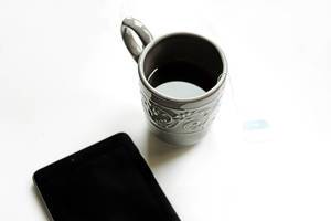 Tea in a grey cup and smartphone on a white background