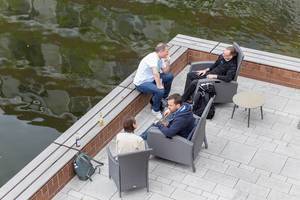 Teilnehmer des Barcamps OMWest zum Thema Onlinemarketing entspannen auf Rattanstühlen auf einer Veranda am See des AXA-Gebäudes in Köln