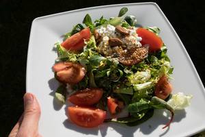 Teller mit gesundem Salat in der Hand. Zutaten: Mangold, Tomaten, Frischkäse, Mandeln und Leinsamen