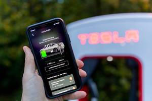 Tesla Supercharging auf einem Smartohone in der App vor einer Tesla Ladestation