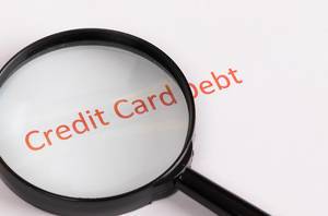 Text Credit Card Debt unter einer Lupe auf weißem Hintergrund