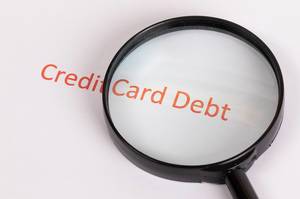 Text Credit Card Debt unter einer schwarzen Lupe auf weißem Hintergrund