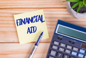 Text Financial Aid auf einer Haftnotiz mit Kugelschreiber, Taschenrechner und Tischpflanze auf einem Holztisch