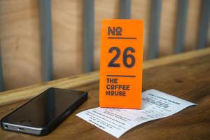 The Coffee House Quittung mit Bestellnummer und einem Smartphone auf einem Tisch