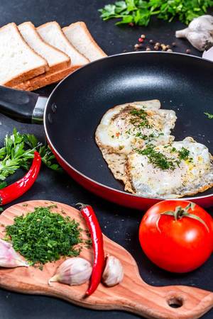 The concept of cooking Breakfast-fried chicken eggs in a frying pan with slices of bread, herbs and vegetables