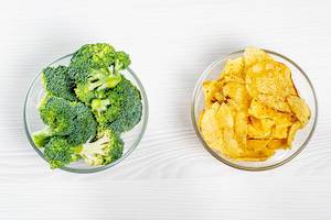 The concept of healthy eating and unhealthy eating is one bowl of broccoli and the other one filled with chips