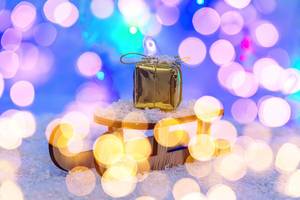 The concept of preparation for winter holidays. Sleigh with gift on snow with bokeh