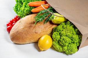 The concept of shopping. Paper bag with fresh bread and vegetables and white wooden background