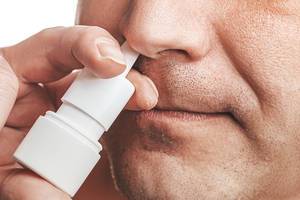 The concept of the treatment of the common cold at home. Male nose and nasal spray close up