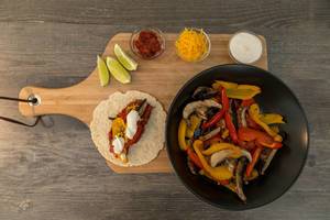 The ingredients for the hello fresh receipt: vegan fajitas with peppers, mushrooms, hot sauce and lime-cream on a cutting board - top view
