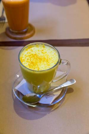 The turmeric drink with ginger "Golden Milk" in a glass with handle and small spoon at vegan "Petit Brot" Restaurant in Barcelona, Spain