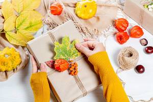 The woman wraps a gift at thanksgiving on autumn background