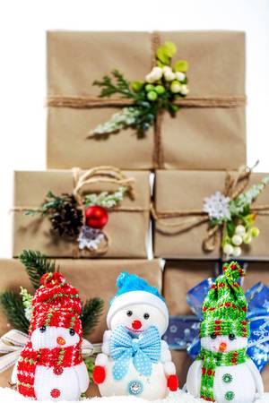 Three little Snowman with scarf and hat in front of stacked christmas presents
