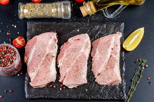 Three raw steaks with ingredients on a black background, top view (Flip 2020)