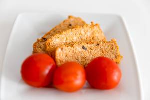 Three red cherry tomatoes in front of vegan Organic Tofu Rosso slices by Taifun, on a white plate