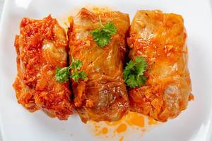 Three stuffed cabbage rolls in tomato sauce on a white plate