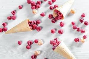 Three waffle cones with red and yellow raspberry on white wooden background (Flip 2019)