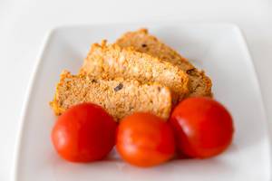 Three washed tomatoes on a white plate, in front of the Mediterranean organic meat substitute "Tofu Rosso" by Taifun