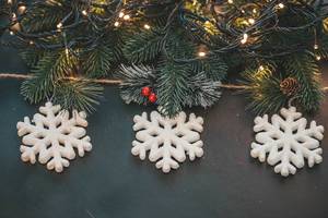 Three white snowflakes with Christmas tree branches and luminous garlands on a dark background (Flip 2019)