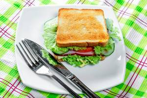 Toast with fried bread, ham and vegetables on a white plate with knife and fork