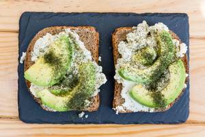 Toast with ricotta and avocado served on serving plate stone