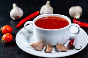 Tomato soup in a tureen on a dark background with garlic, cherry tomatoes and garlic