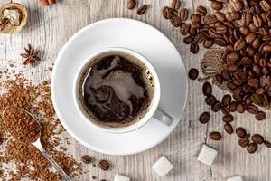 Top view a cup of hot coffee with whole and ground grains, sugar and spices on a wooden background (Flip 2019)