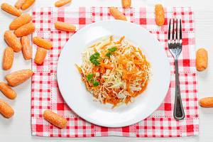 Top-view auf Karotten- und Krautsalat auf einem Teller, umgeben von kleinen, frischen Karottemn