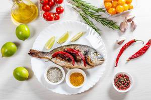 Top view baked Dorado fish with spices and vegetables on white wooden background (Flip 2019)