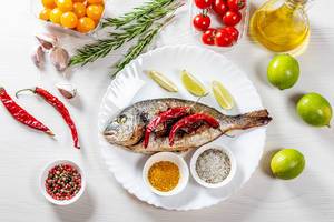 Top view baked Dorado fish with spices and vegetables on white wooden background