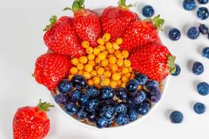 Top view, bowl of oatmeal, strawberries, blueberries and sea buckthorn berries on a white background